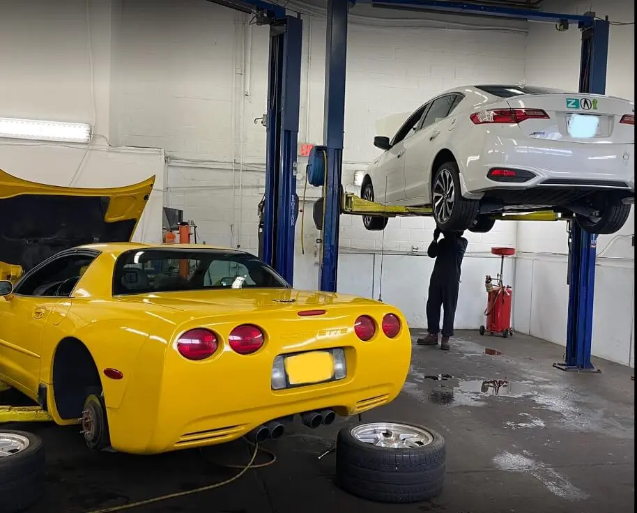 Yellow Corvette and a white sedan on lifts inside the KMF Automotive shop